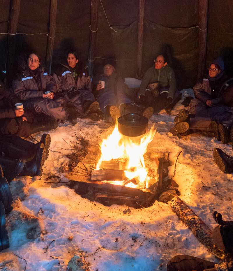 grupo de viajantes ao redor de fogueira dentro de tenda na Noruega