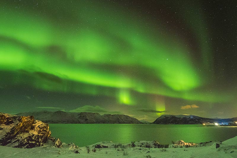 Aurora boreal sobre um lago com cidade ao fundo na Noruega