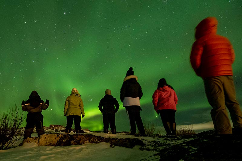 Viajantes contemplando a aurora boreal durante uma viagem pela Noruega
