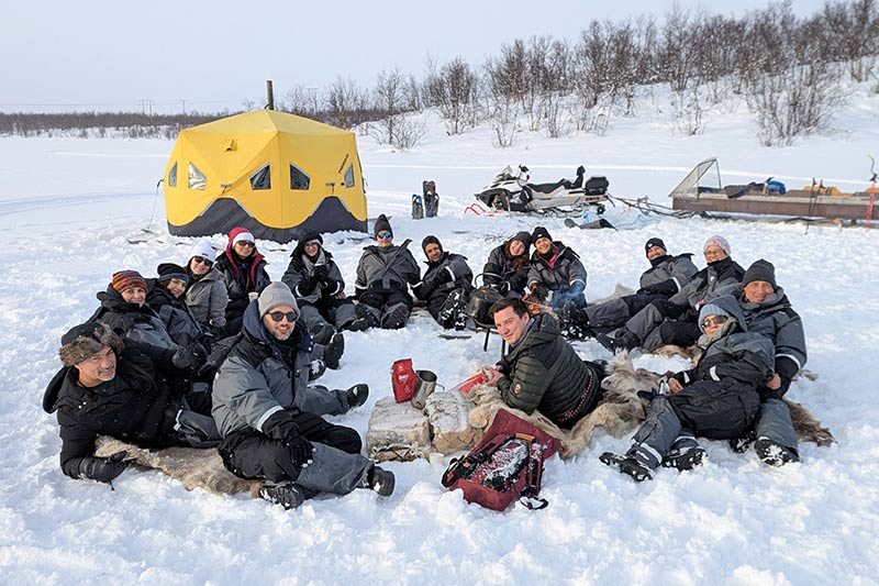 Viajantes sentados na neve durante uma viagem pela Noruega, com barraca ao fundo